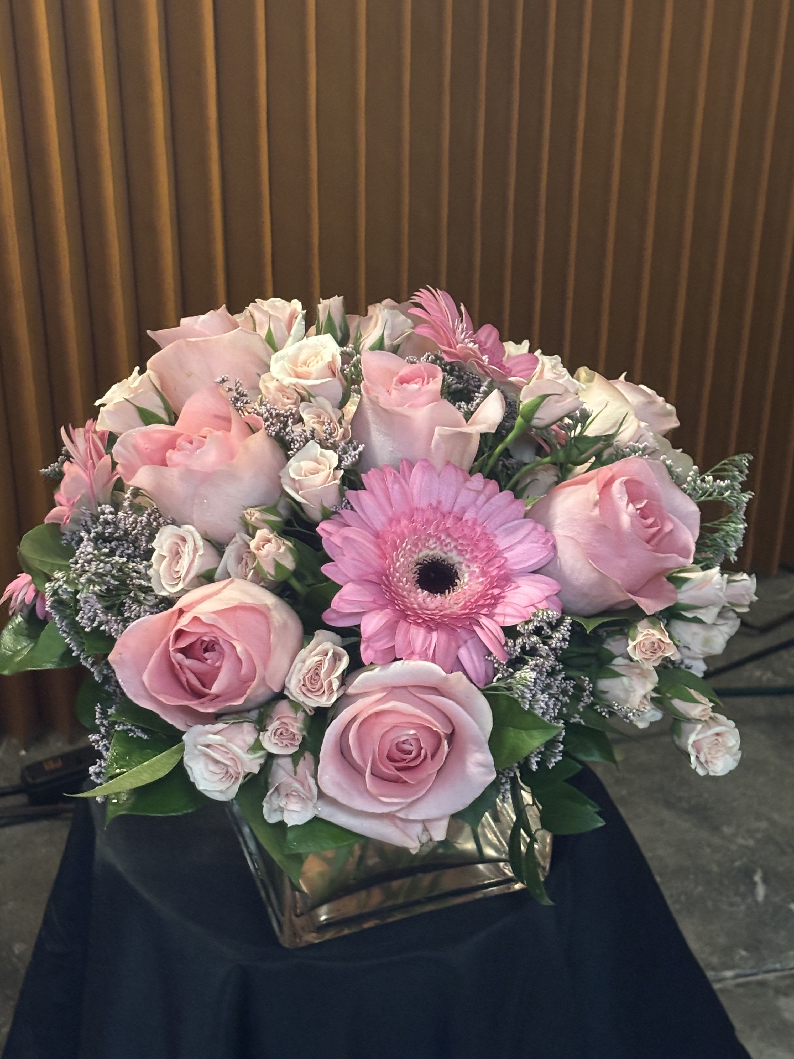 Pink roses and a gerbera daisy arranged in a square vase