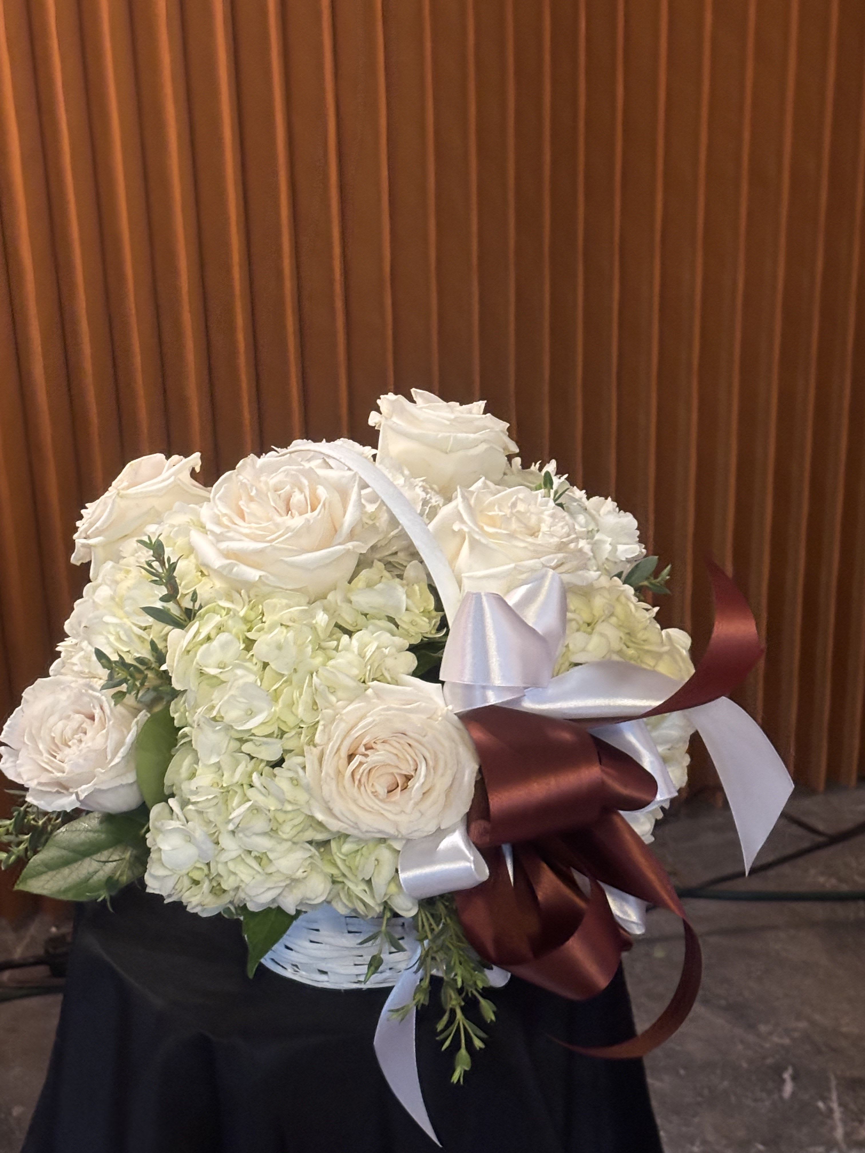 White rose and hydrangea bouquet in a basket with satin ribbons