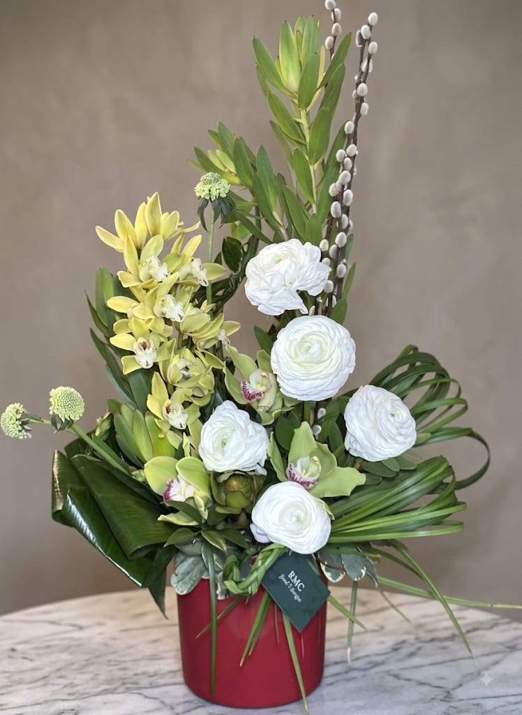 Tall floral arrangement with white blooms and yellow orchids in a red vase