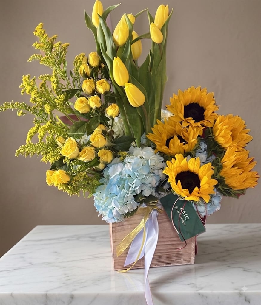 Yellow tulips, roses, sunflowers, and blue hydrangeas in a wooden box