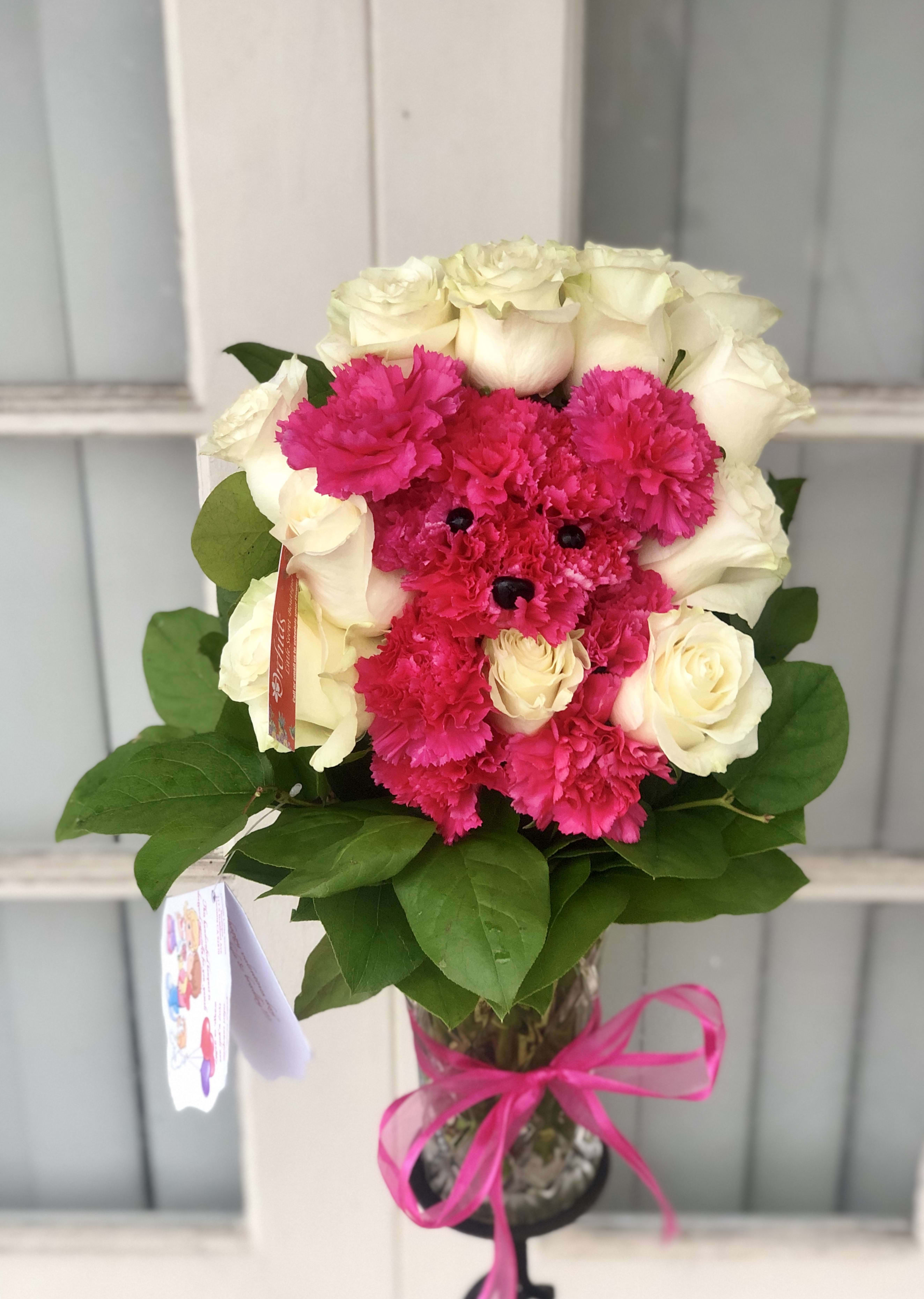 Pink carnations and white roses arranged in a glass vase with a ribbon