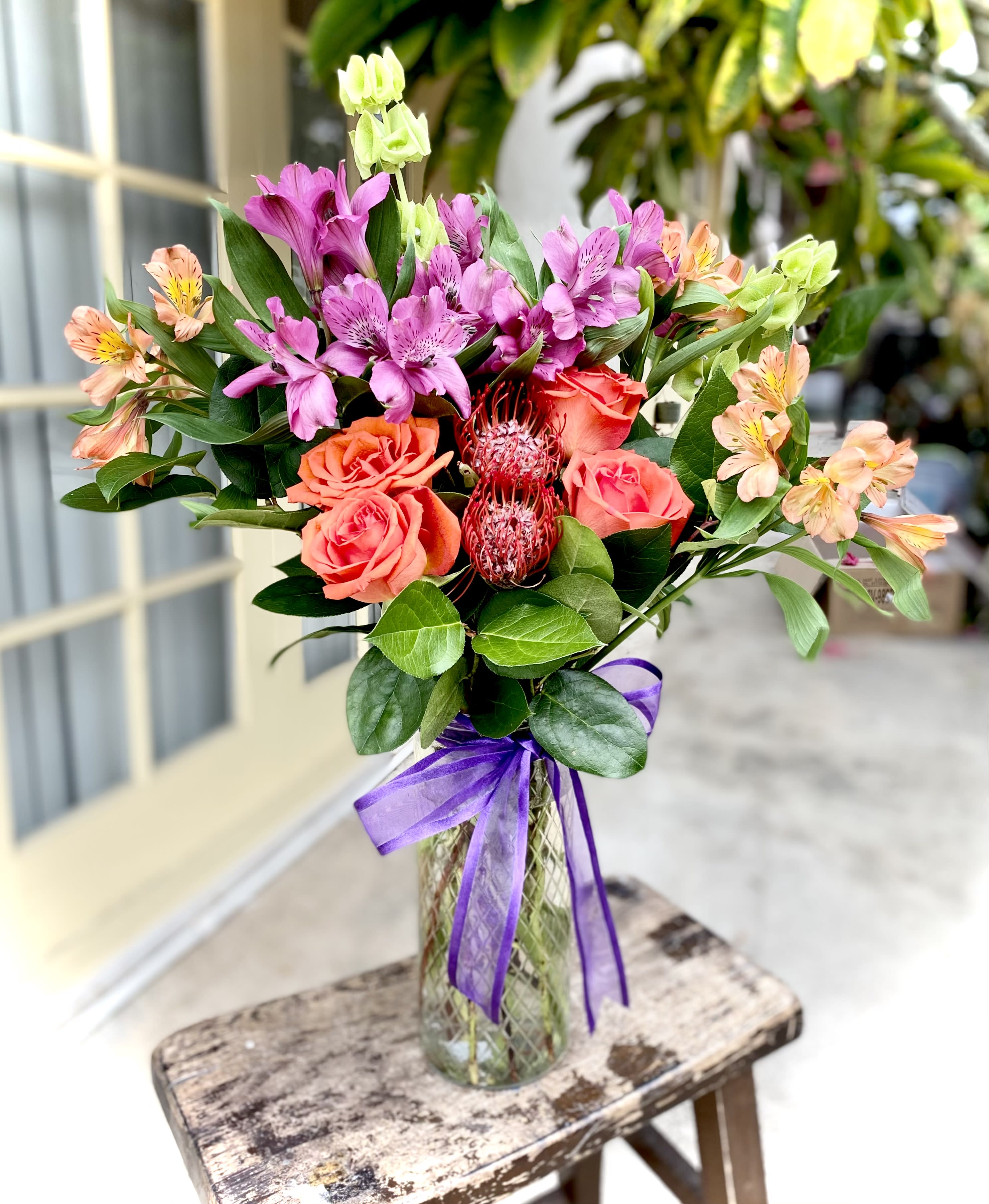 Mixed bouquet of pink and orange flowers in a glass vase with a purple ribbon
