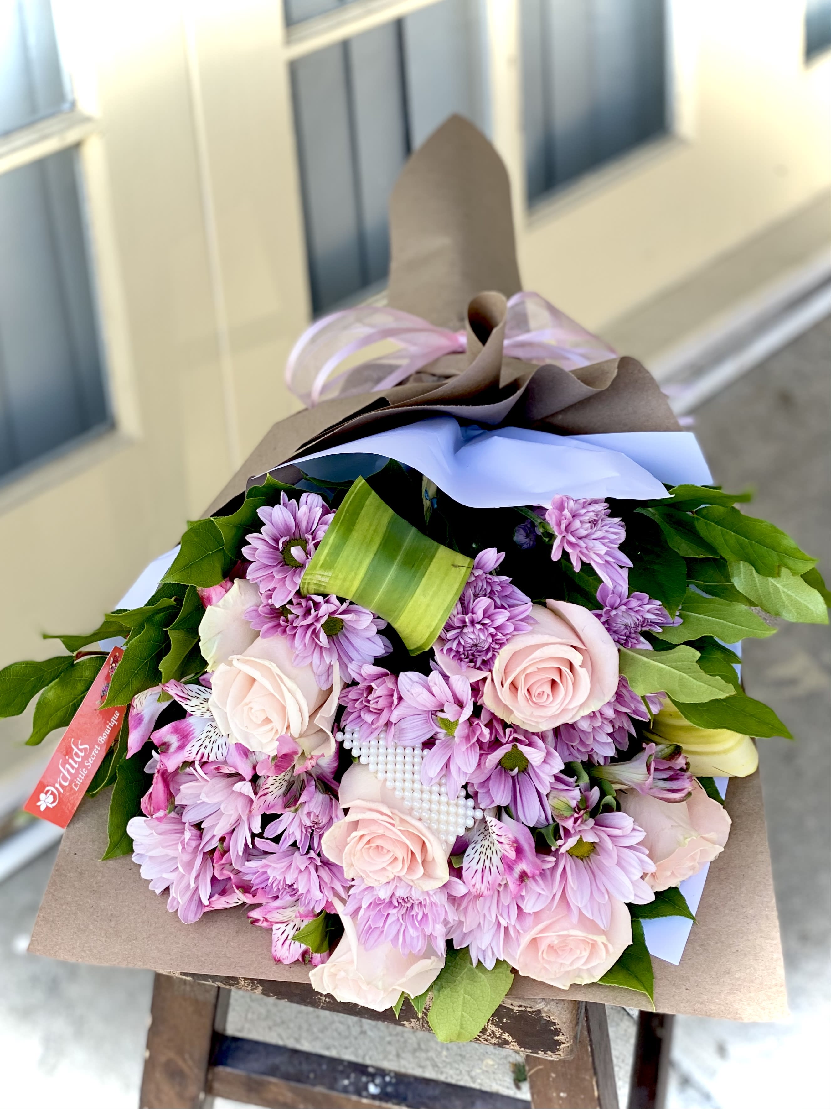 Bouquet of pink roses and purple daisies wrapped in brown paper