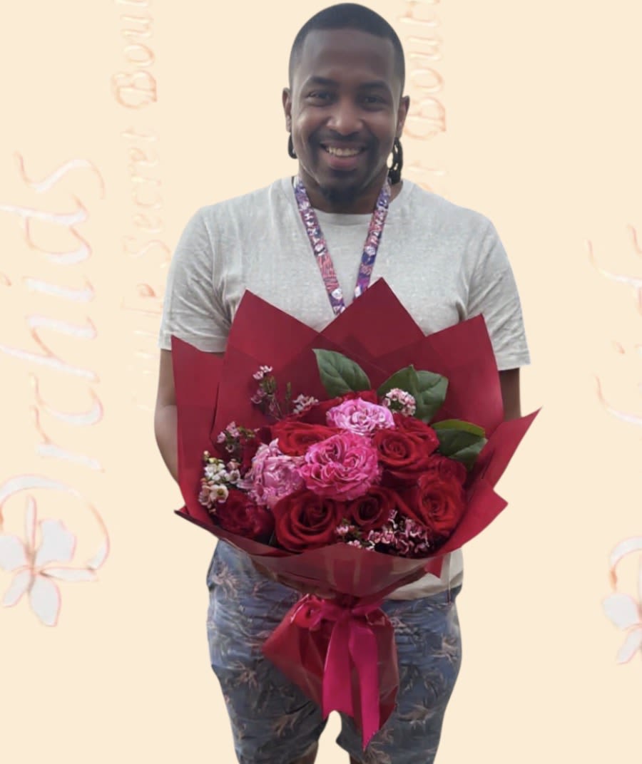 Man holding a bouquet of red and pink roses wrapped in burgundy paper