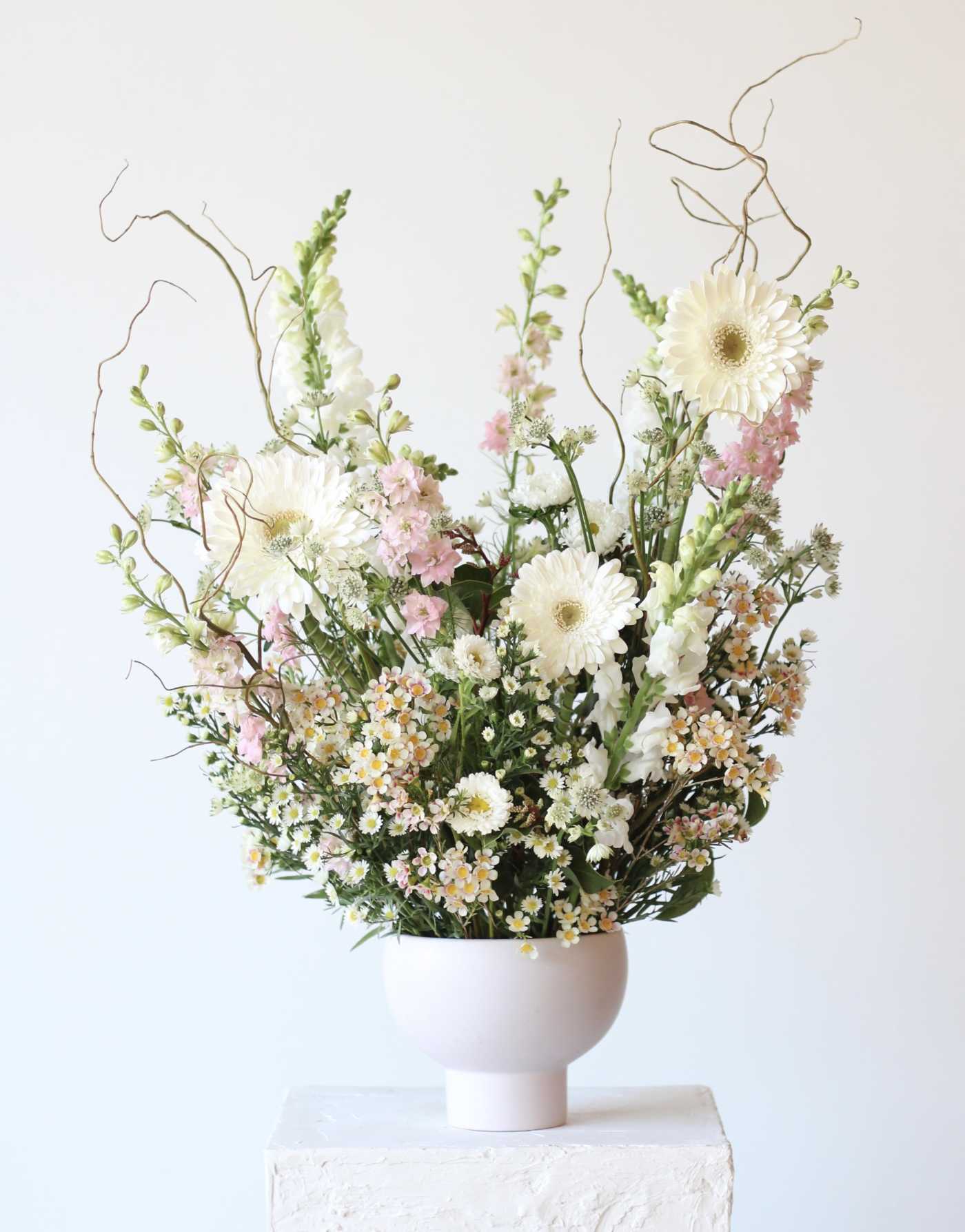 Tall floral arrangement with white daisies and pink blooms in a white vase