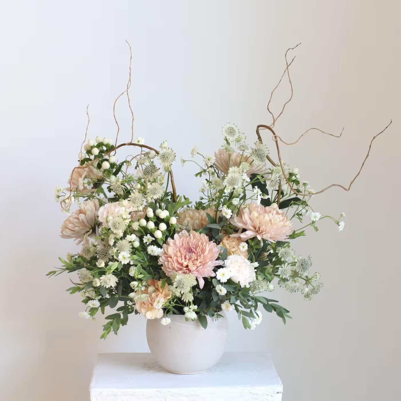 Blush and white floral arrangement in a white vase with curly branches