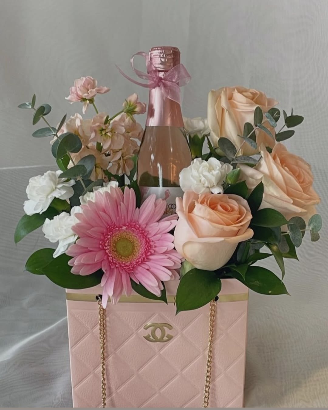 Pink floral arrangement with roses and a champagne bottle in a pink gift bag