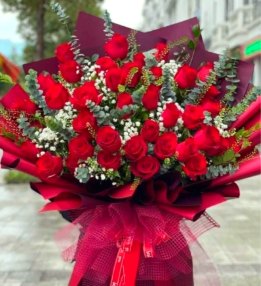 The "Grand Elegance" 50-Rose Bouquet - "A breathtaking showstopper featuring 50 premium red roses layered with delicate baby's breath and fresh eucalyptus. Wrapped in luxury matte burgundy paper with a textured mesh bow, this massive bouquet is the ultimate statement of romance and luxury."
