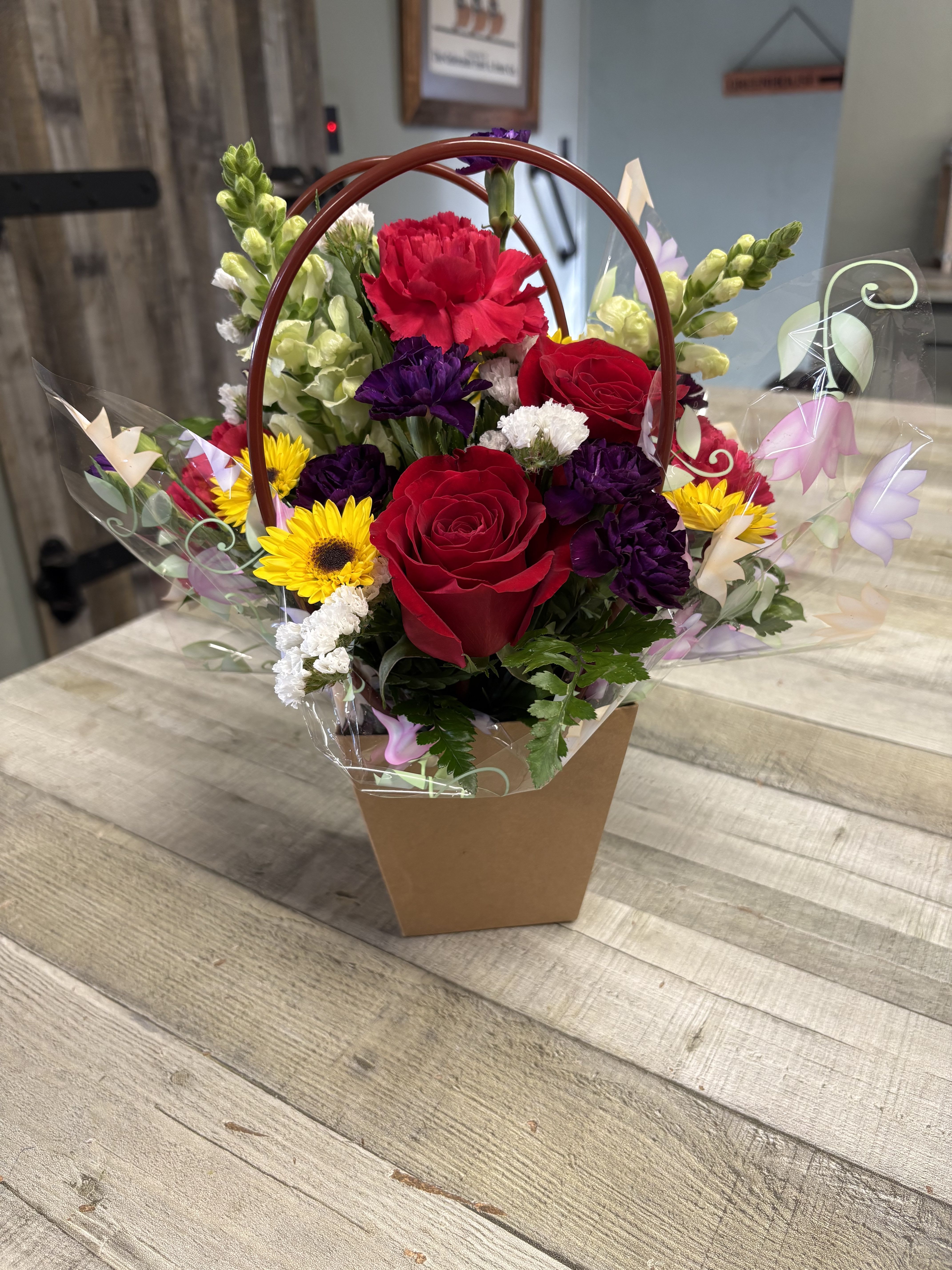 Mixed bouquet with red roses, yellow daisies, and purple flowers in a handled box