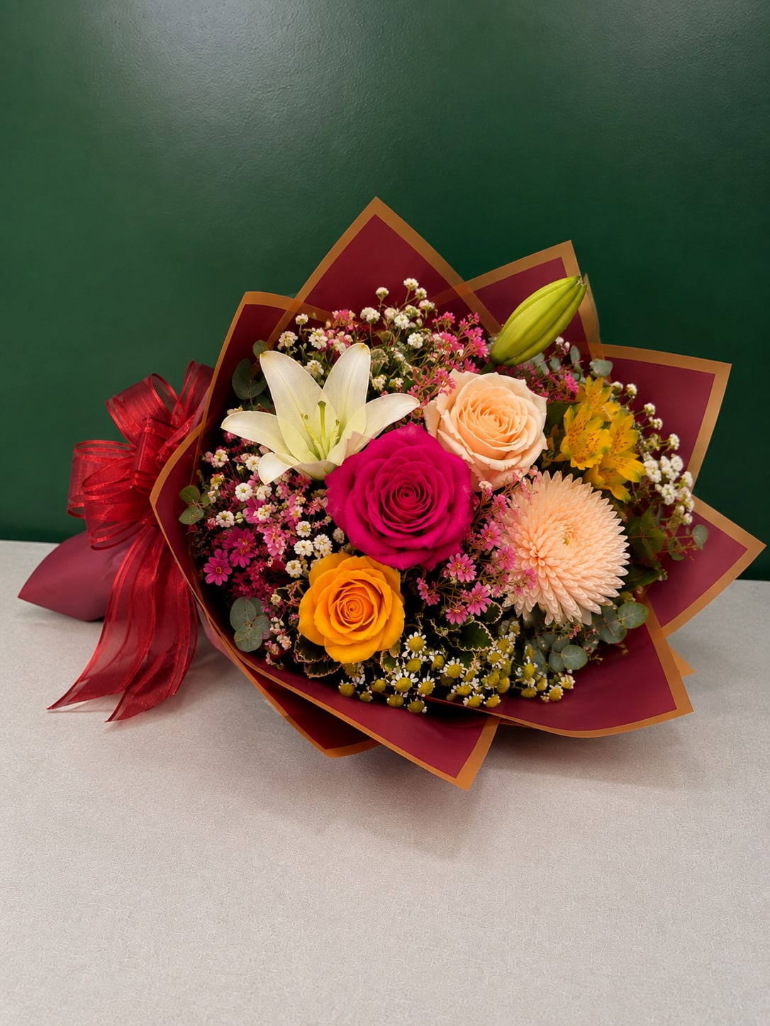 Mixed bouquet with roses, lilies, and a chrysanthemum wrapped in burgundy paper