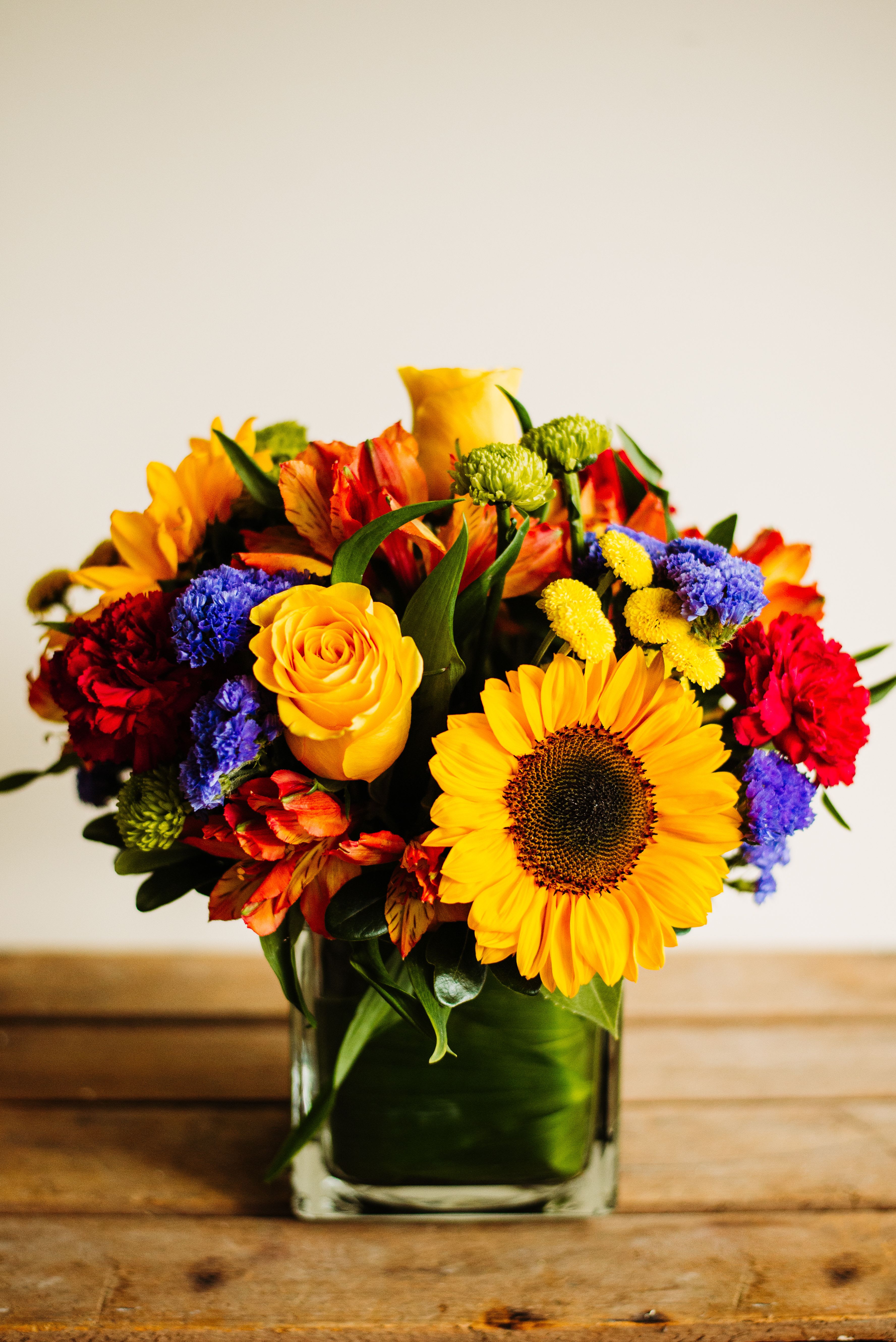 Golden Hour Glow - Bring the warmth of the setting sun indoors with Golden Hour Glow. Bursting with sunflowers, golden roses, fiery alstroemeria, and vibrant accents of red and violet, this arrangement captures the magic of late-day light. Perfect for brightening a home, celebrating a milestone, or simply spreading a little joy.
