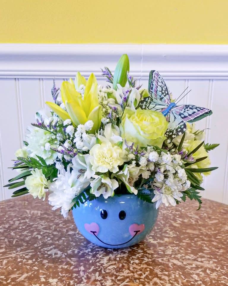 Yellow and white flower arrangement in a blue smiley-face bowl with a butterfly decoration