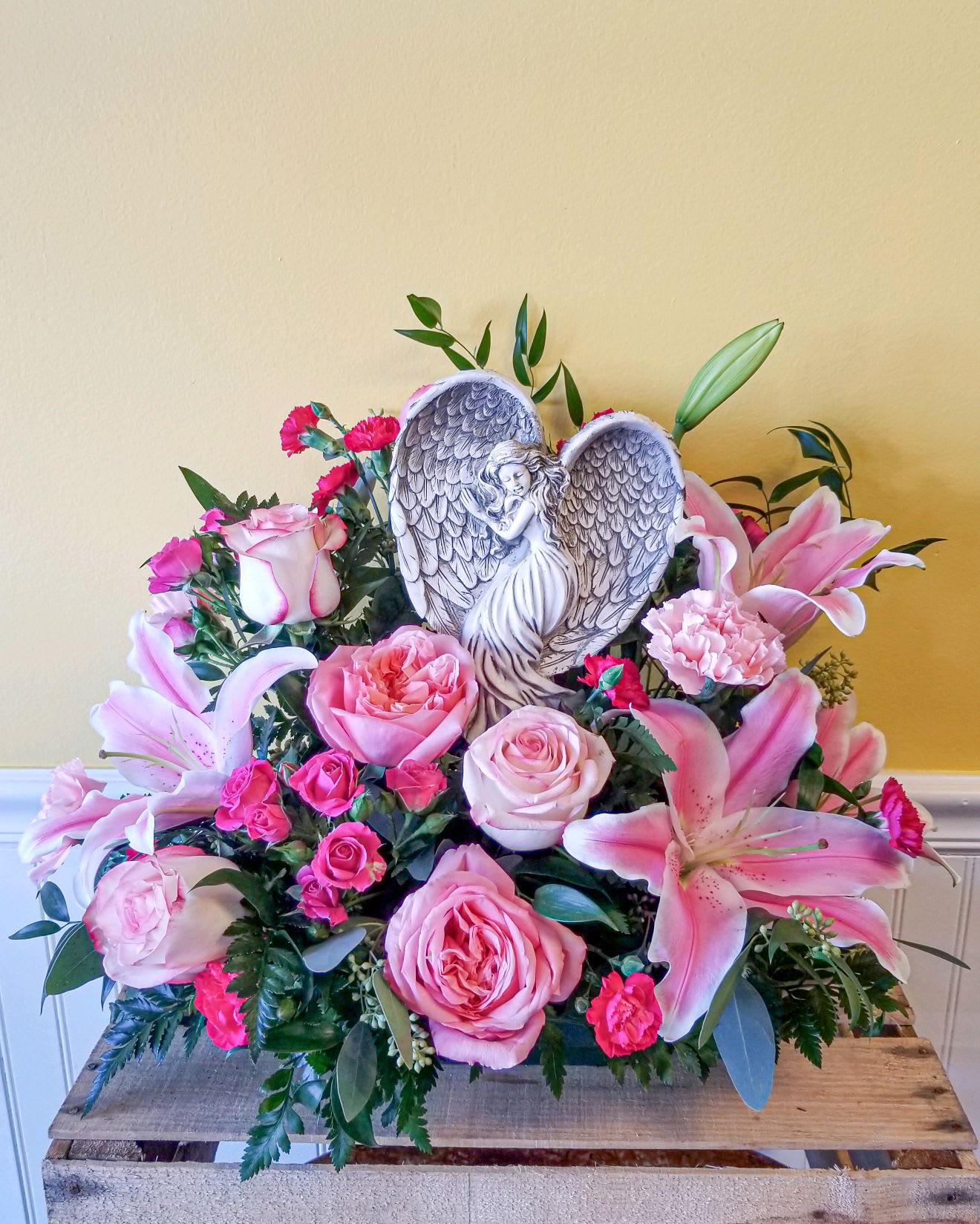 Pink roses and lilies arranged around a heart-shaped angel plaque