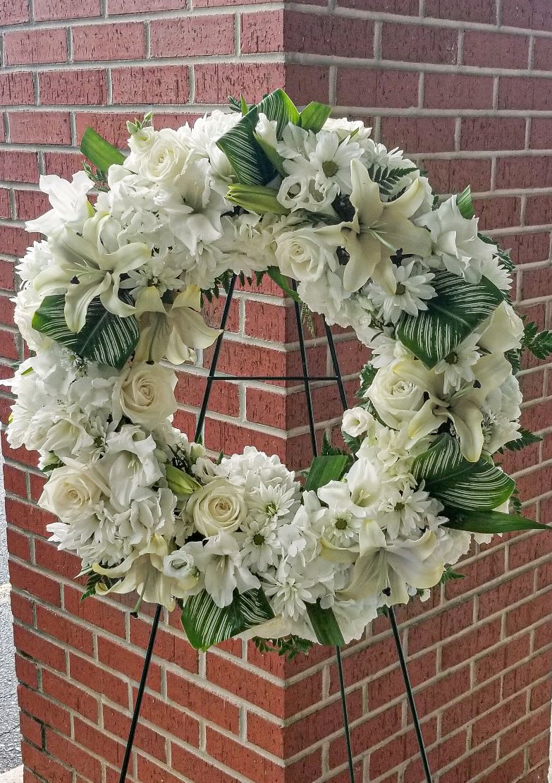 White floral wreath on a black stand against a brick wall
