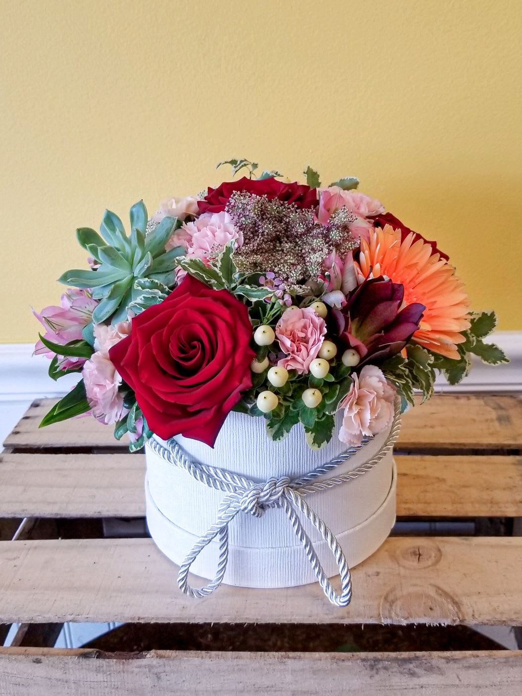 Mixed flower arrangement in a white round box with a rope bow