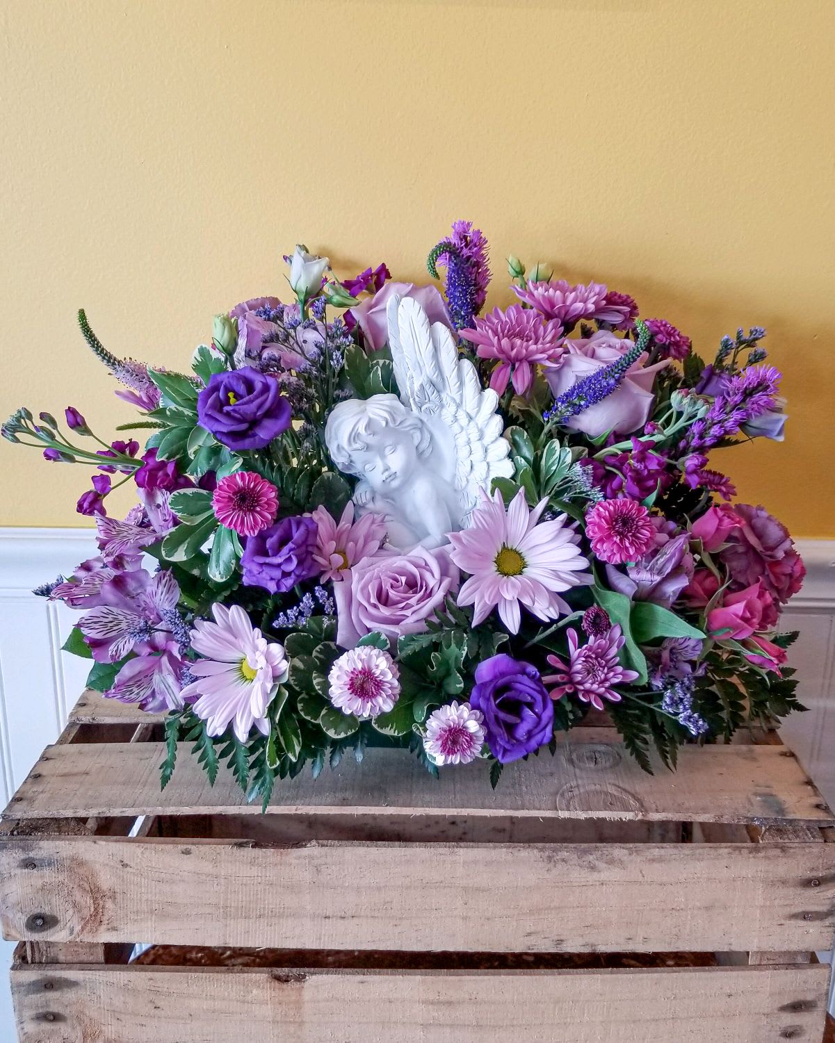 Purple and pink floral arrangement with a white angel figurine