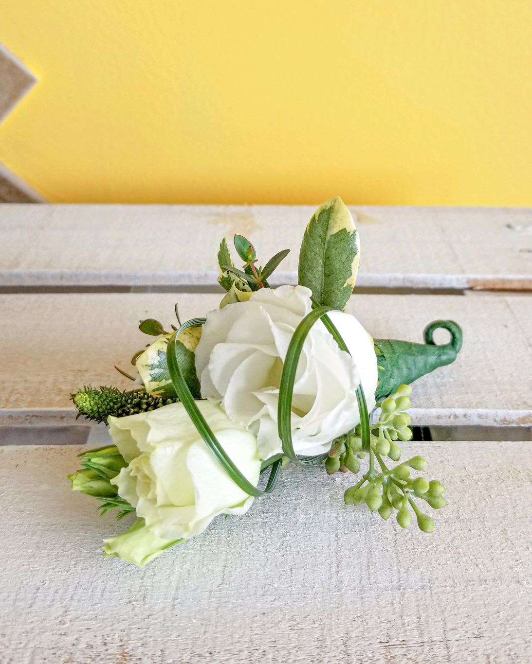 White rose boutonniere with green accents and berries