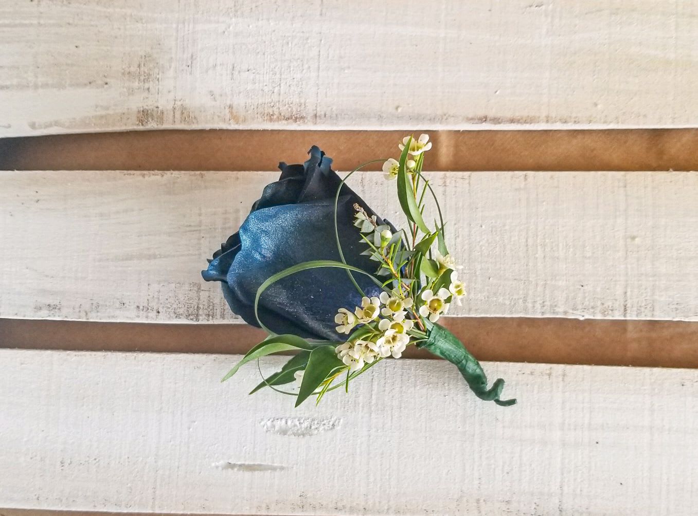 Dark blue rose boutonniere with small white flowers and greenery
