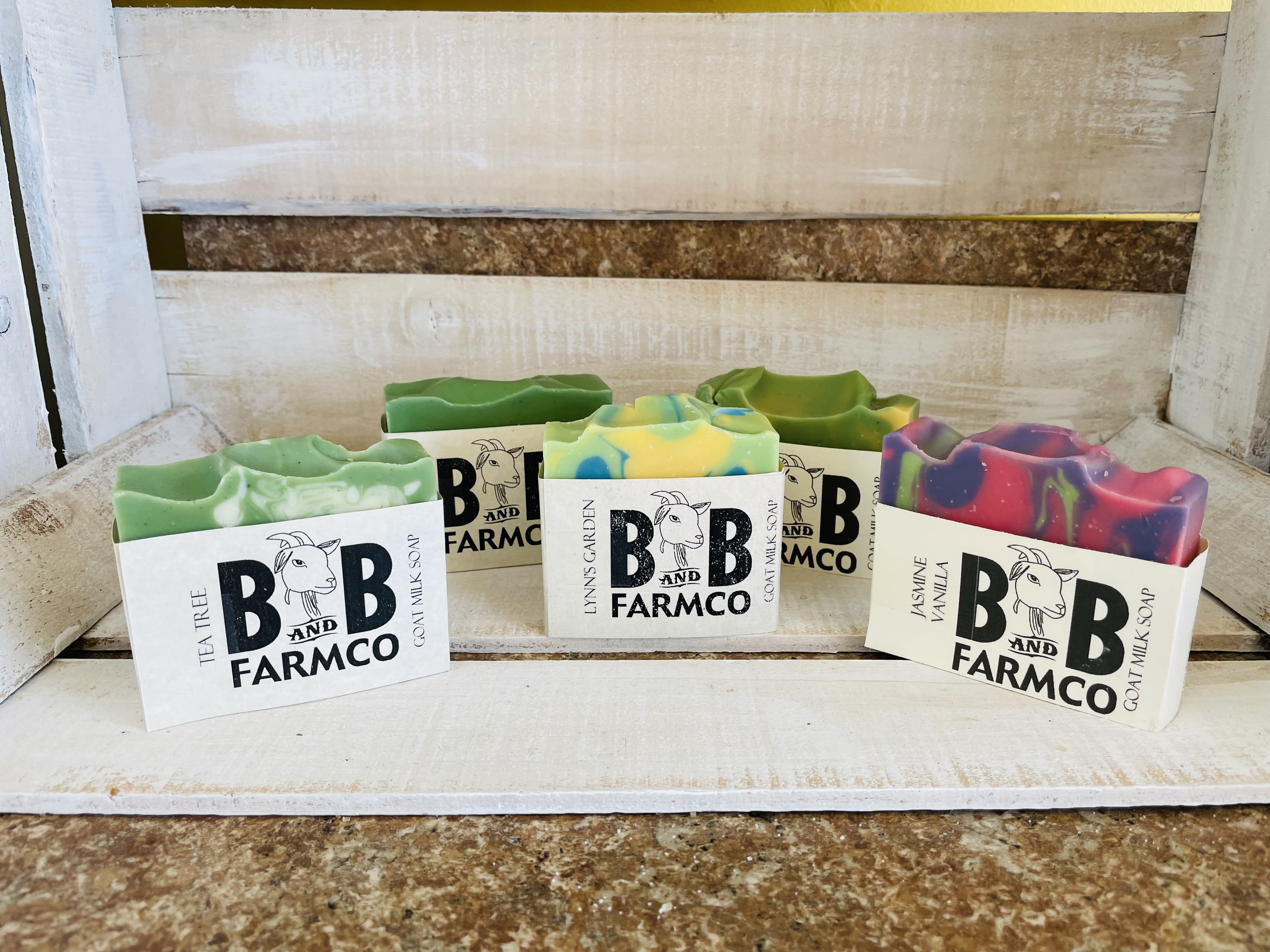 Five bars of colorful goat milk soap on a rustic shelf