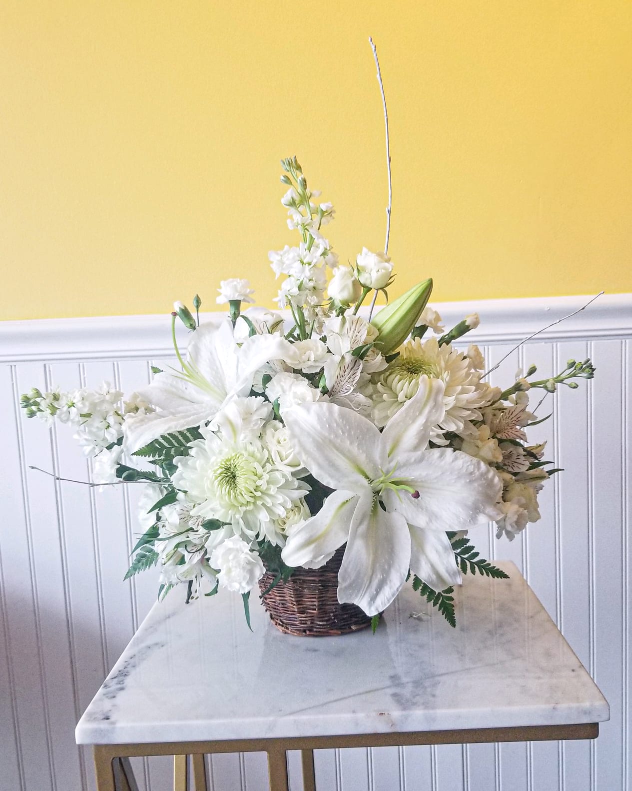 White floral arrangement in a wicker basket with lilies and chrysanthemums