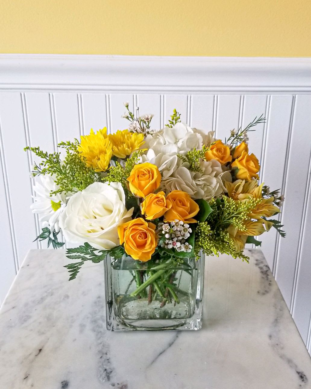 Yellow and white flower arrangement in a square glass vase