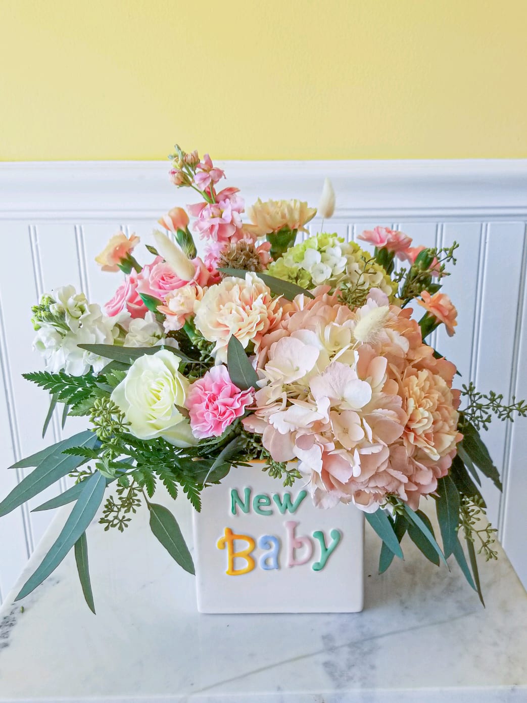 Pastel flower arrangement in a white vase with "New Baby" text