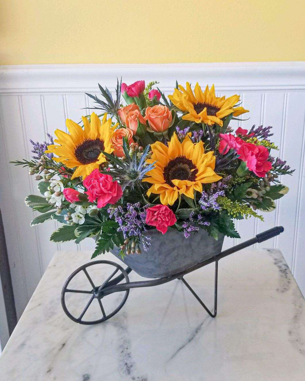 Sunflowers, roses, and carnations arranged in a wheelbarrow planter