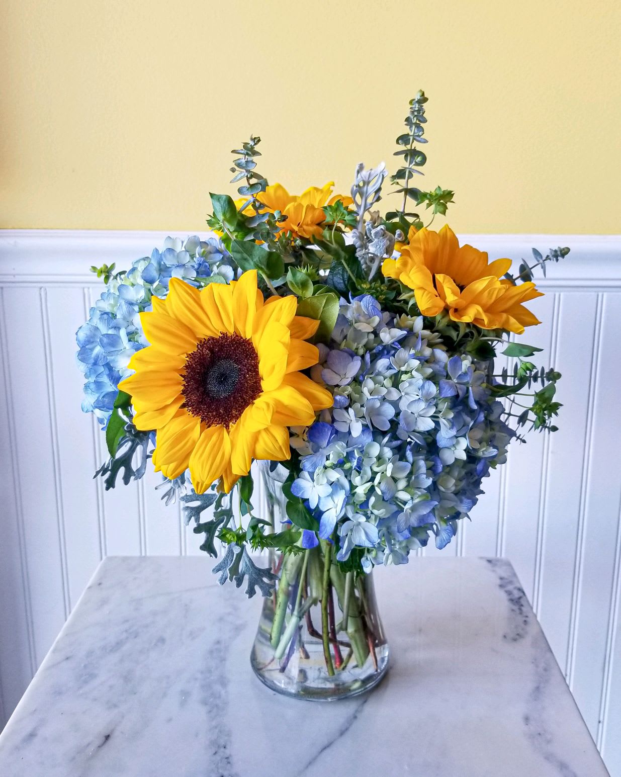 Sunflowers and blue hydrangeas arranged in a clear glass vase