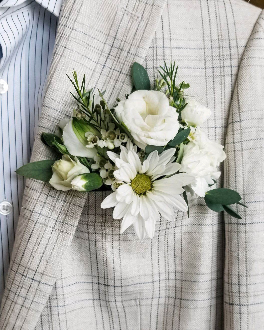 White boutonniere with daisy and rose blooms on a plaid jacket