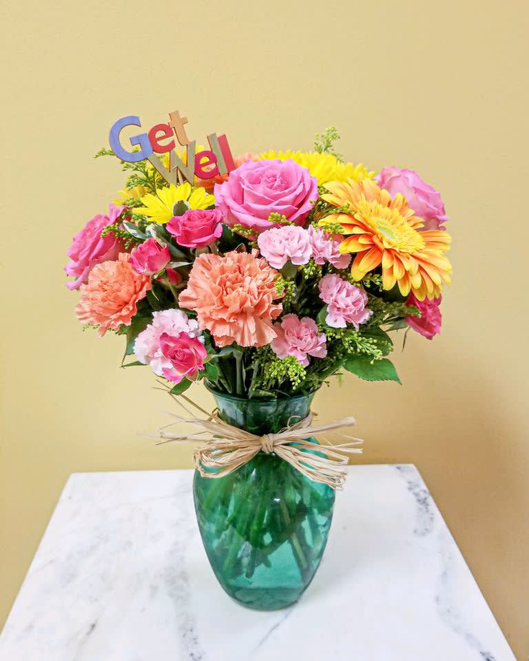 Colorful bouquet in a green glass vase with a "Get Well" sign