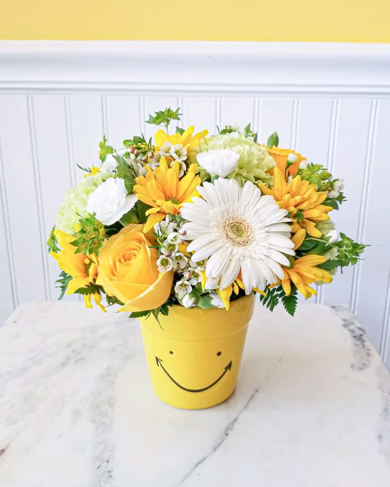 Yellow and white flower arrangement in a smiley-face pot
