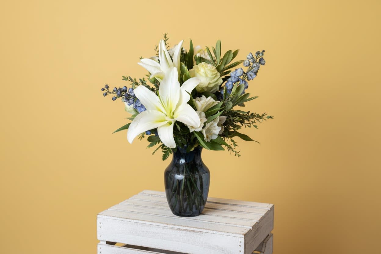 Healing Love - White lilies and roses take center stage in this calming sympathy or thoughtful-gift arrangement, titled for its gentle, restorative feel. The white-and-blue color story-soft blue delphinium spikes and green foliage-creates a serene, uplifting presence that's perfect for comforting someone or marking a quiet celebration such as a remembrance, get-well, or simple "thinking of you" moment. Approx 16in X 12 in