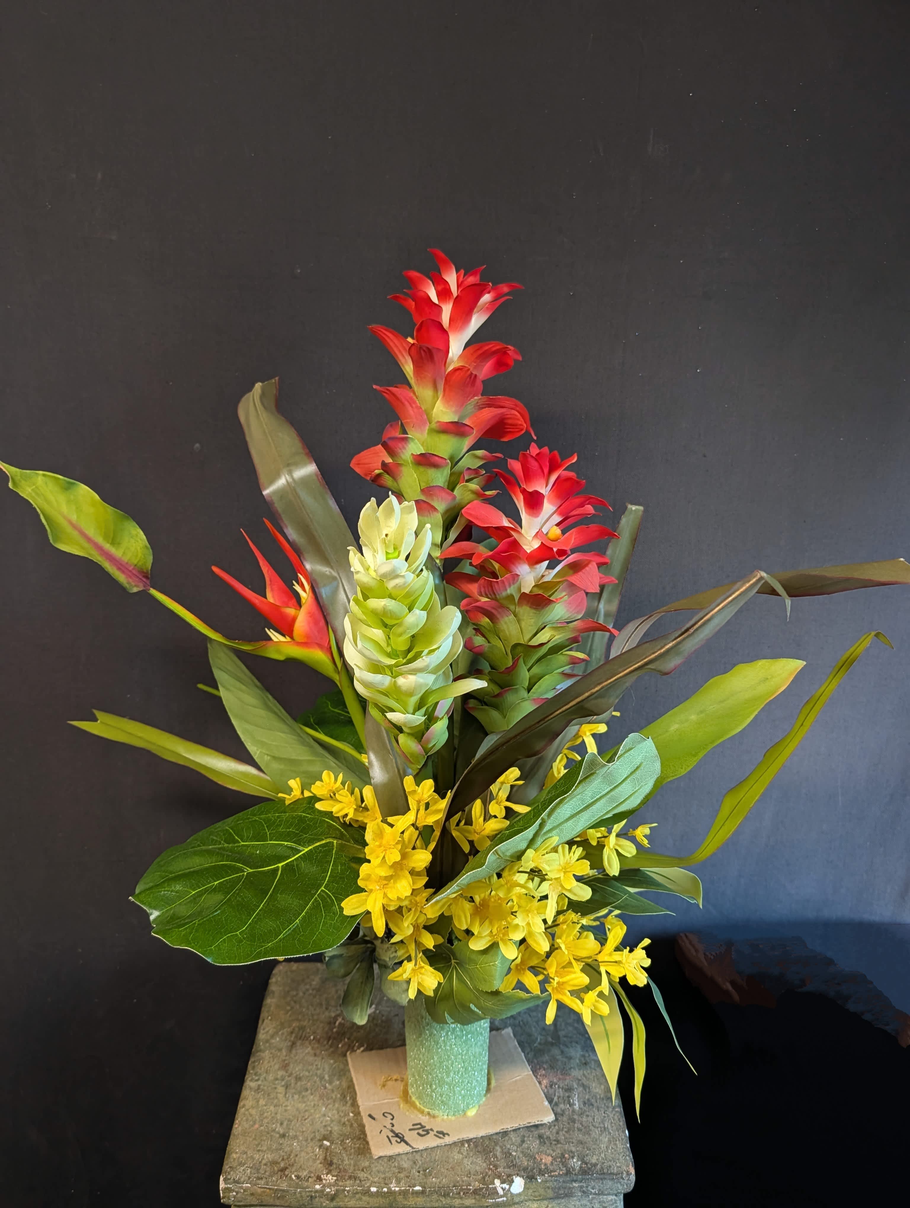 Tropical arrangement with red and green blooms in a teal vase