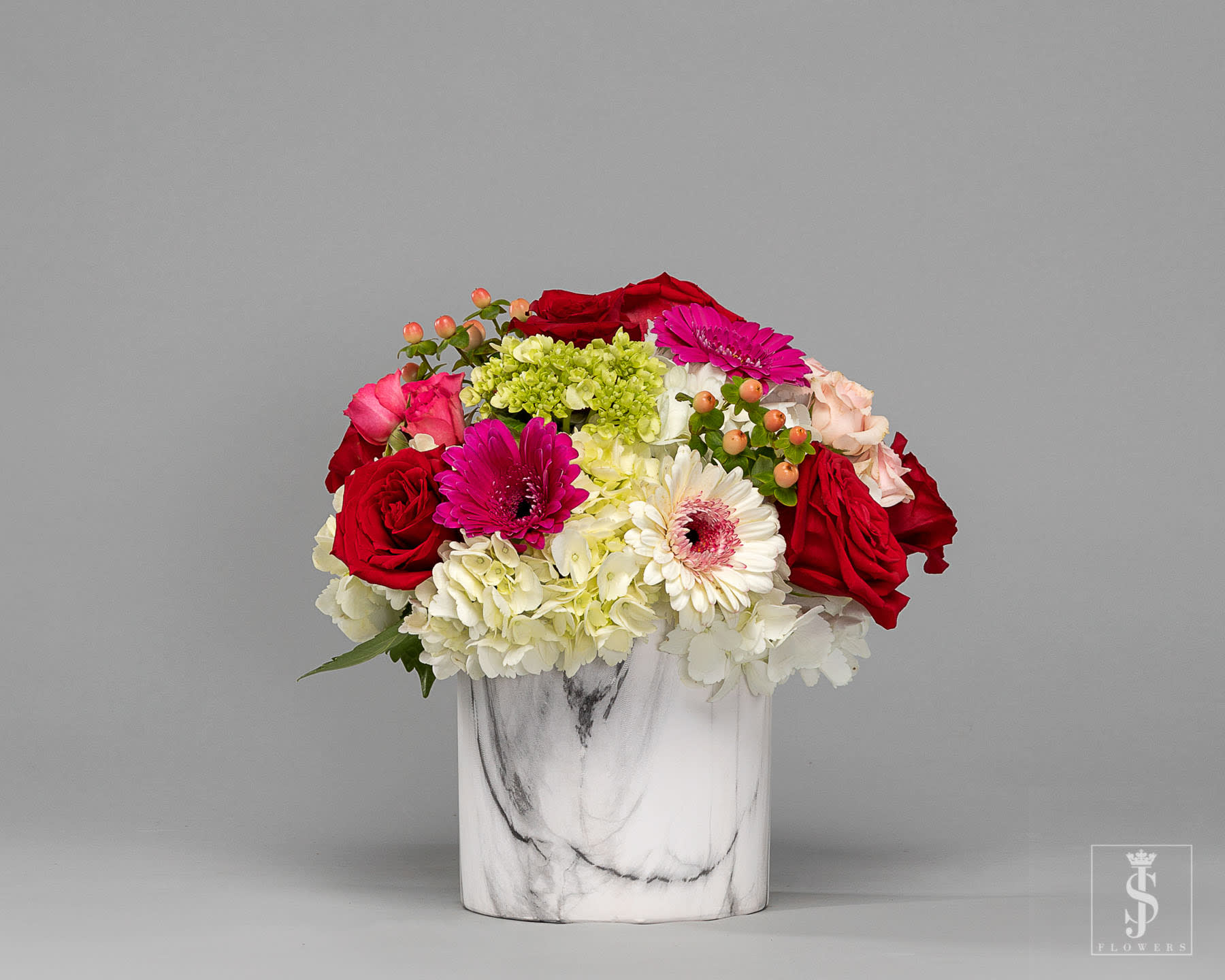 Mixed bouquet of red roses, pink gerberas, and white hydrangeas in a marble vase