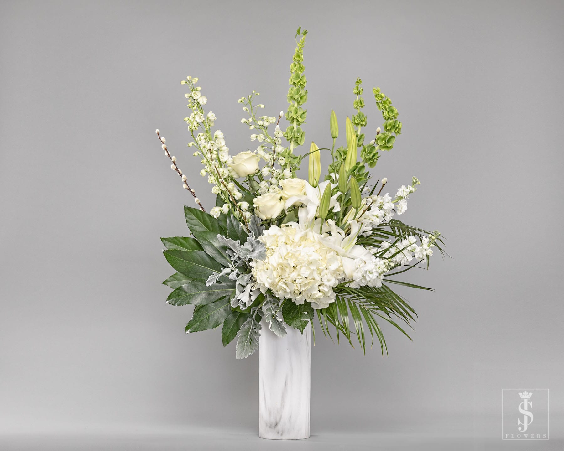 White floral arrangement in a tall marble vase with green accents
