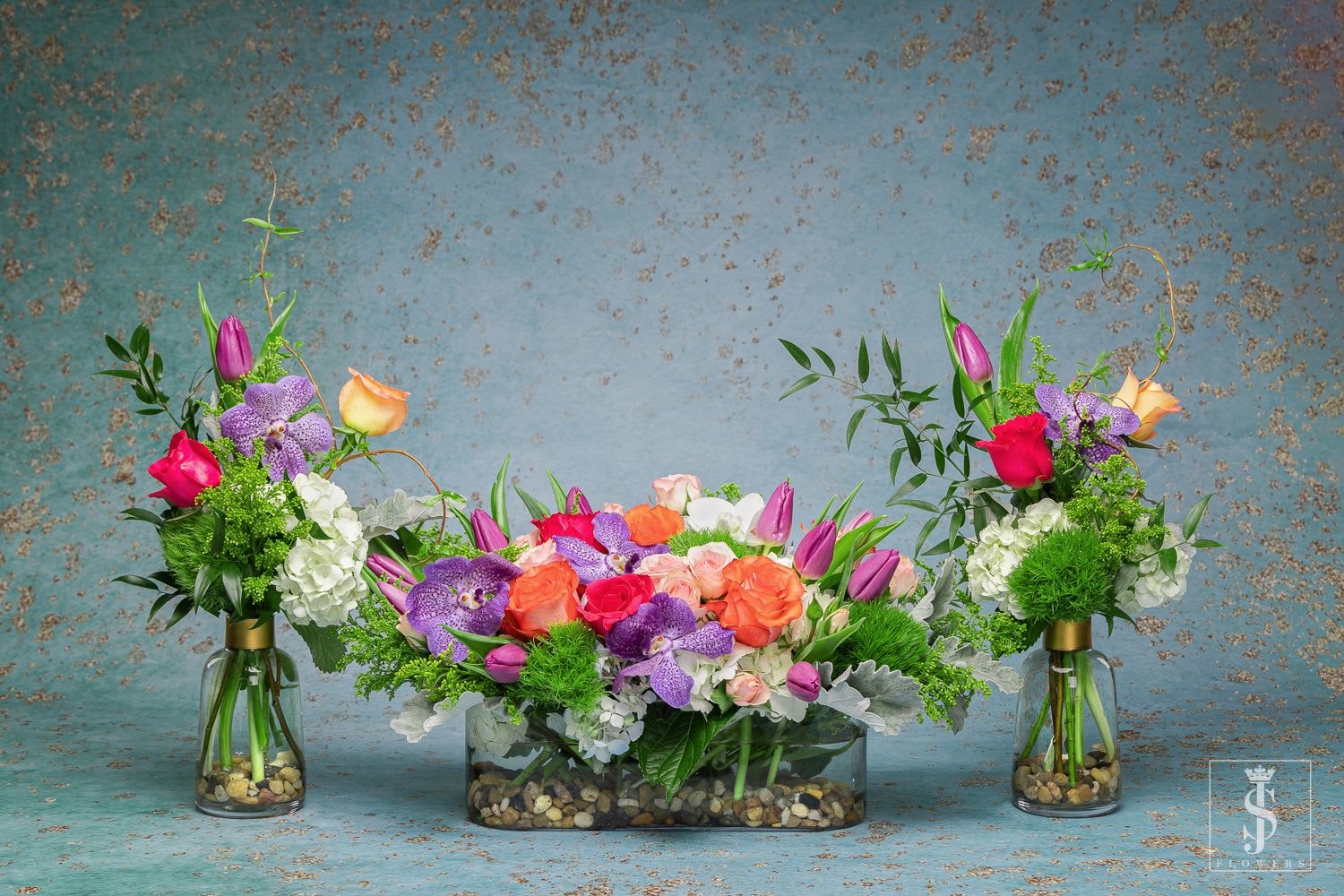 Three colorful floral arrangements in glass vases and a low rectangular container