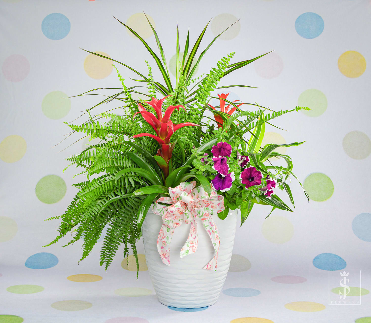 Tropical floral arrangement in a white vase with pink ribbon