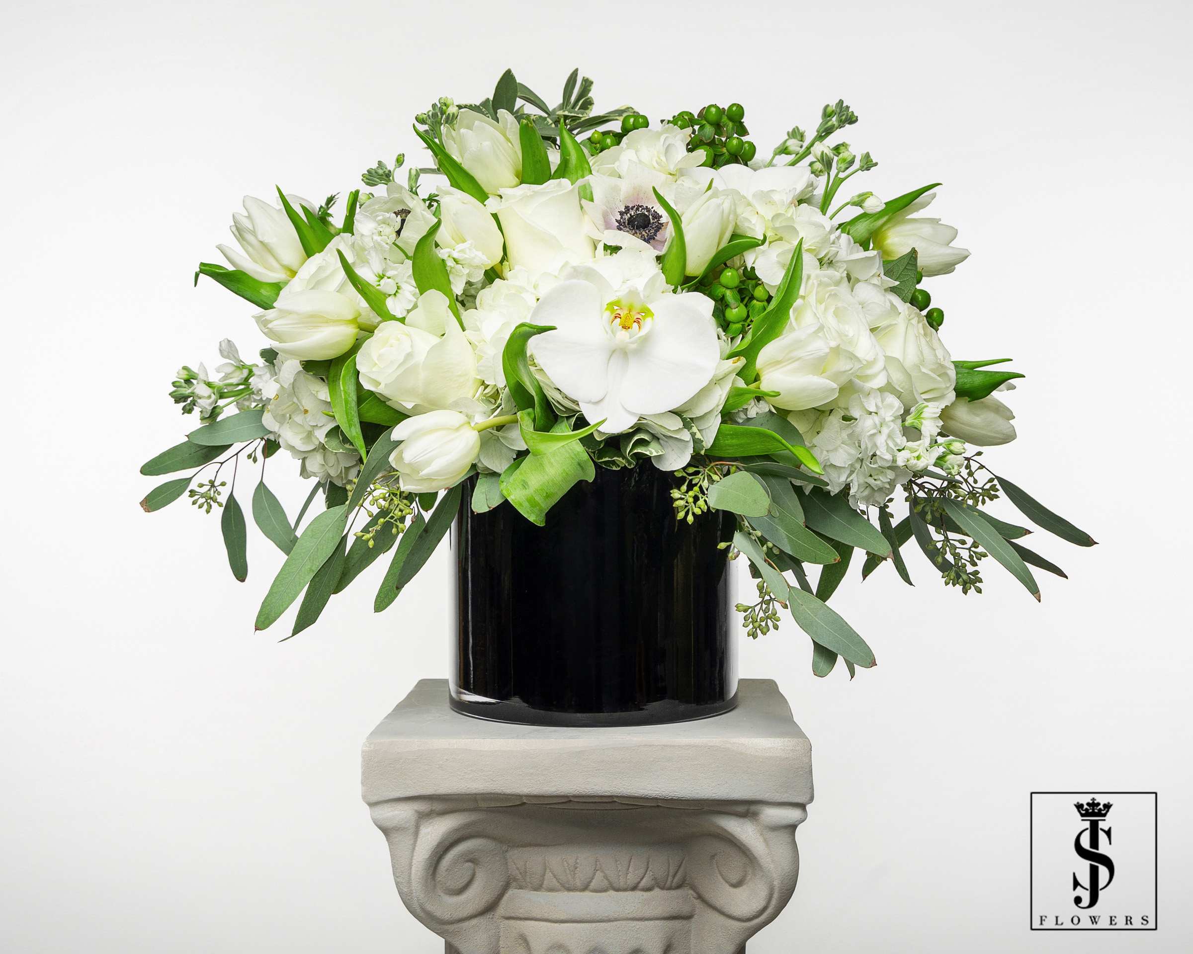 White floral arrangement in a black vase with trailing greenery