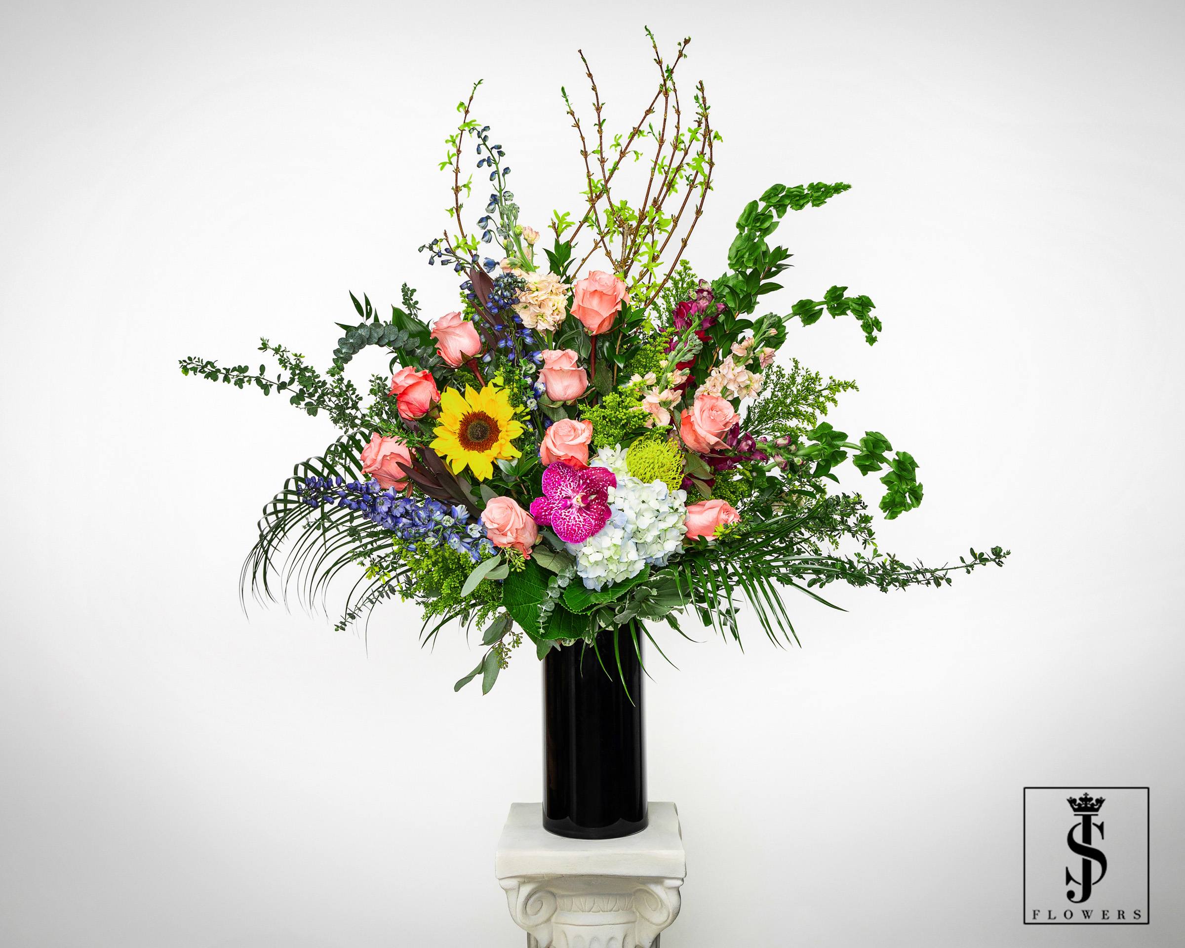 Tall mixed flower arrangement in a black vase with pink roses and a sunflower