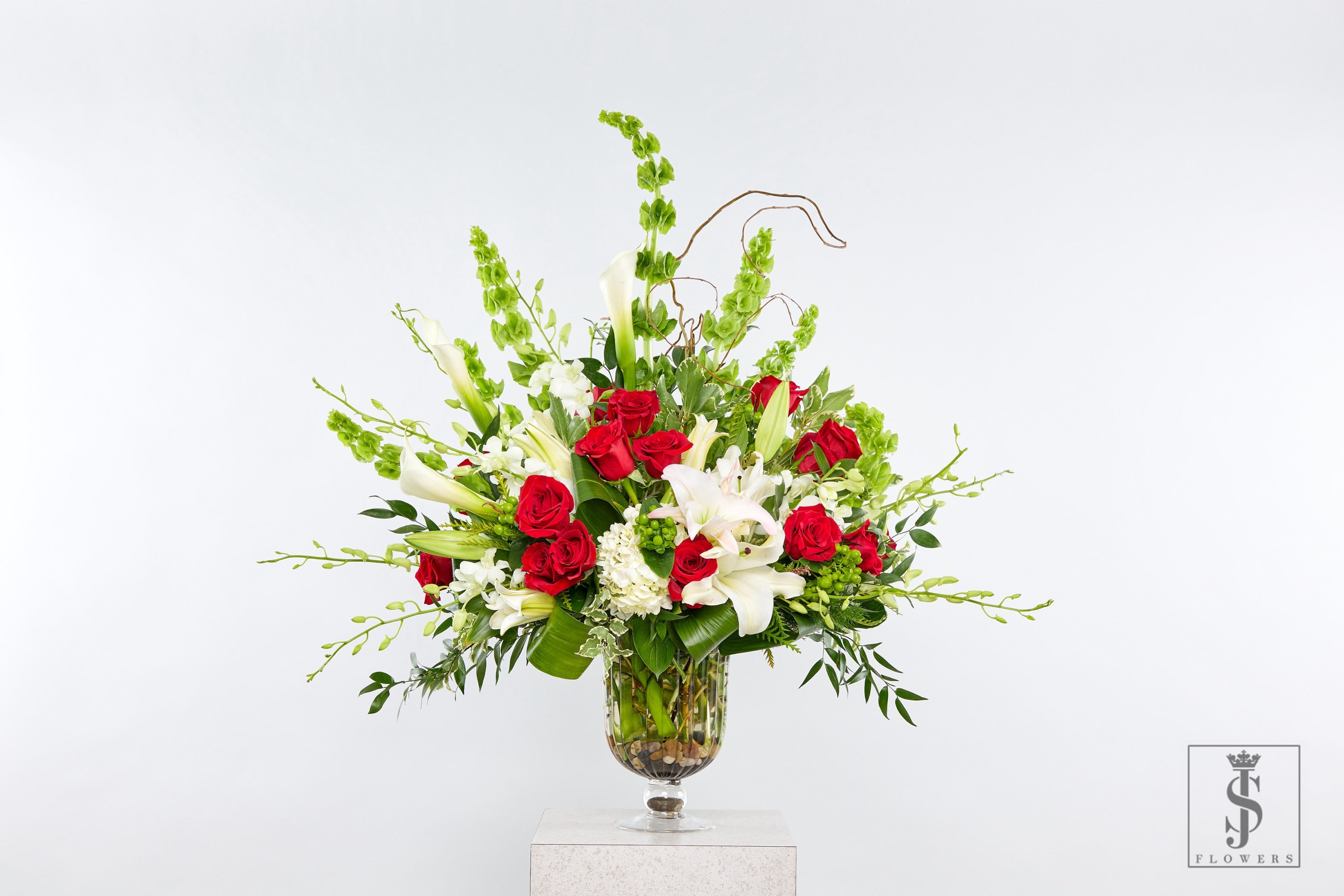 Red roses and white lilies in a glass vase with tall green accents