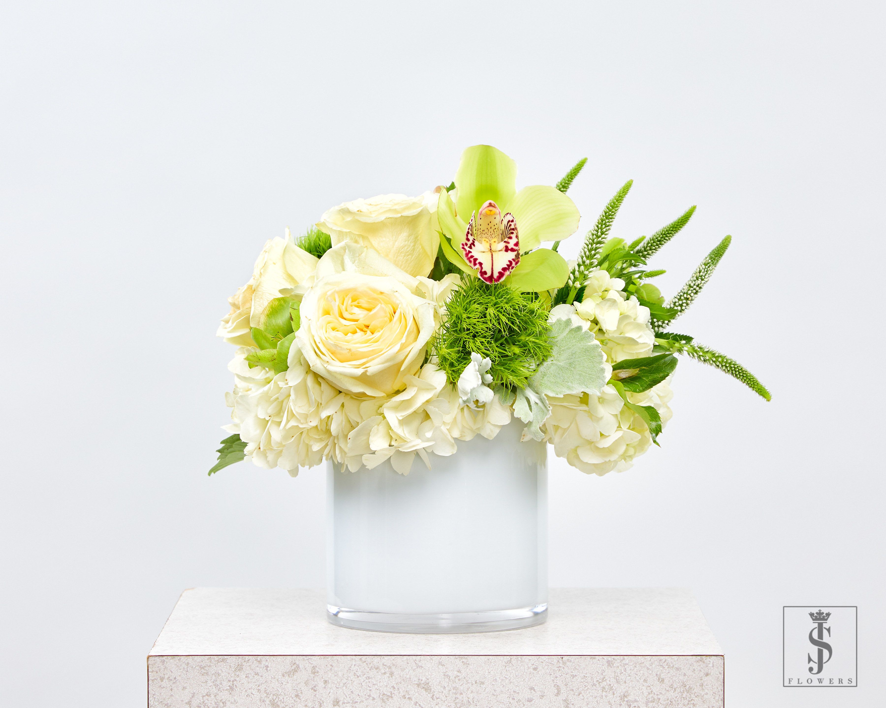 Cream roses and hydrangeas in a clear glass vase with green accents