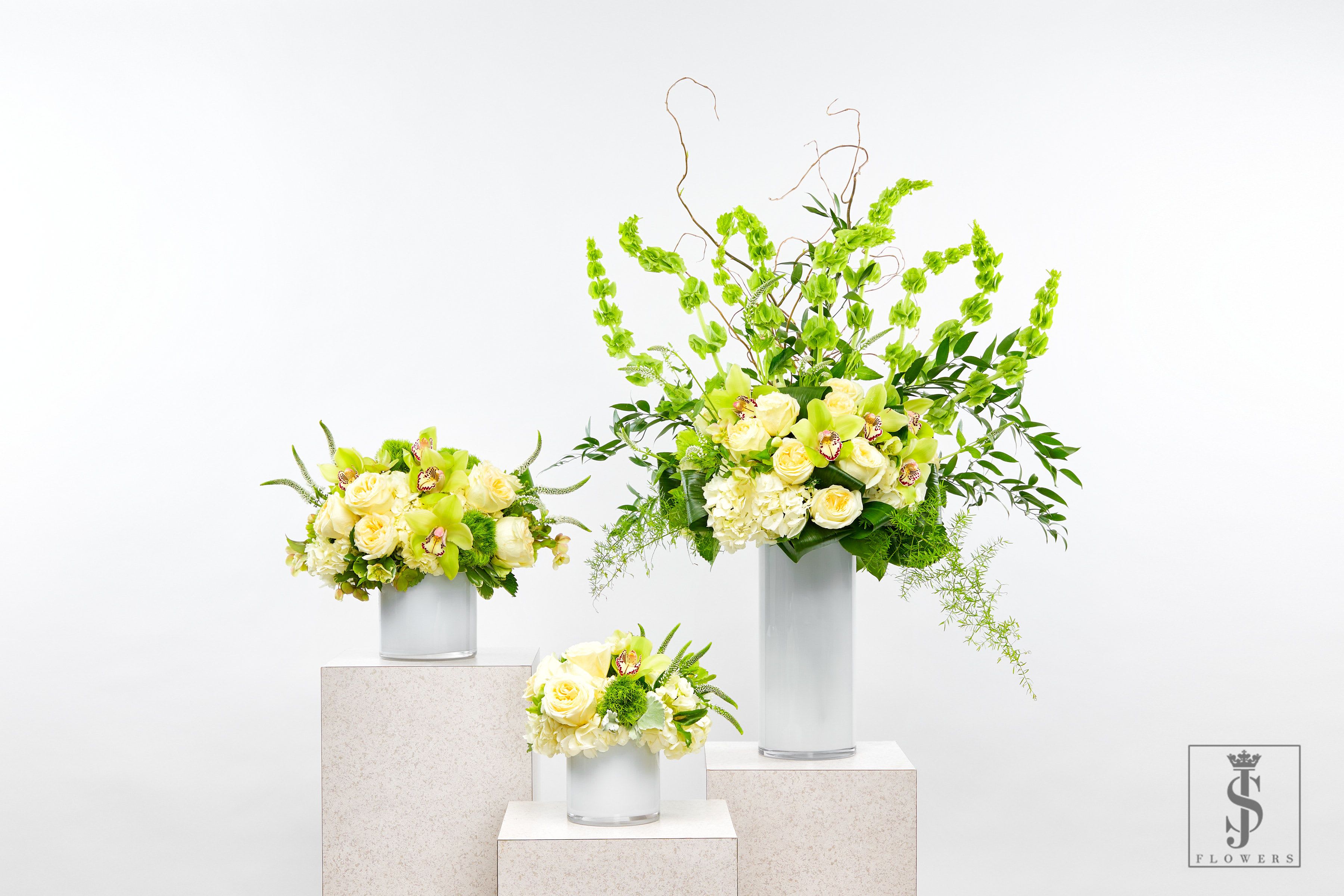 Three pale yellow floral arrangements in silver vases on pedestals