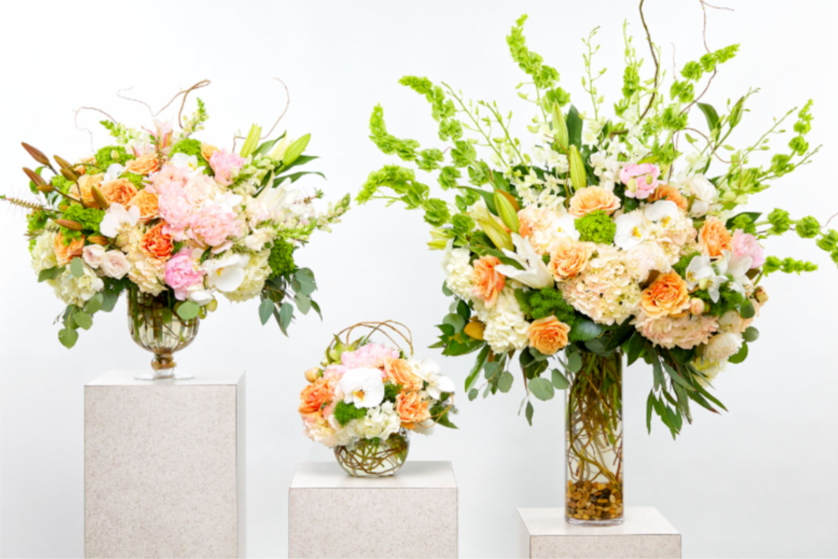 Three pastel floral arrangements in glass vases on white pedestals