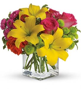 Bouquet of yellow lilies, pink roses, and green pompons in a clear glass vase