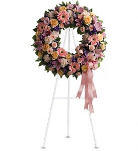 Pastel floral wreath on a white stand with a pink ribbon