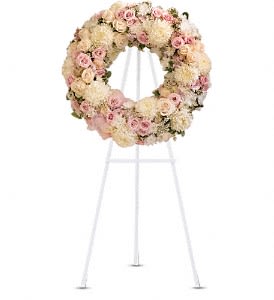Round floral wreath of pale pink and cream flowers on a white stand