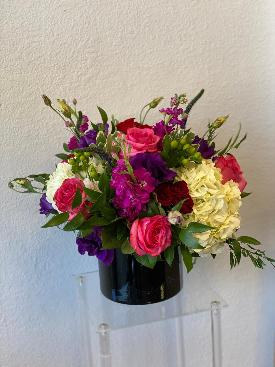 Mixed bouquet of roses, hydrangeas, and purple blooms in a black vase