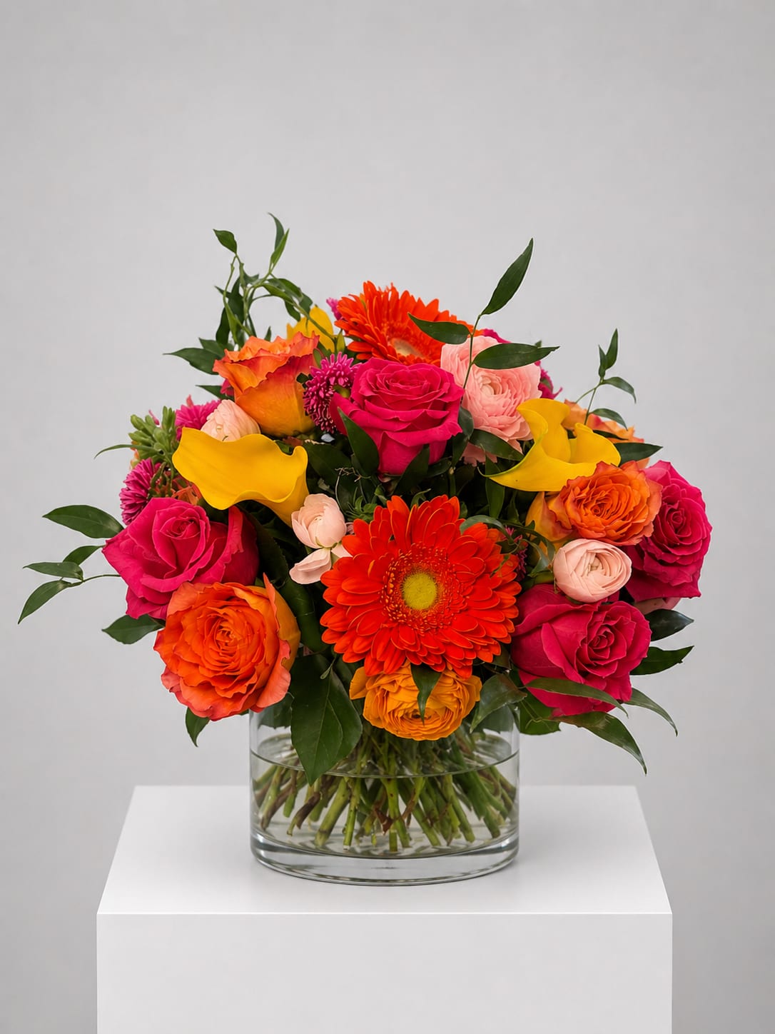 Bright mixed bouquet of roses, gerbera daisies, and calla lilies in a glass vase