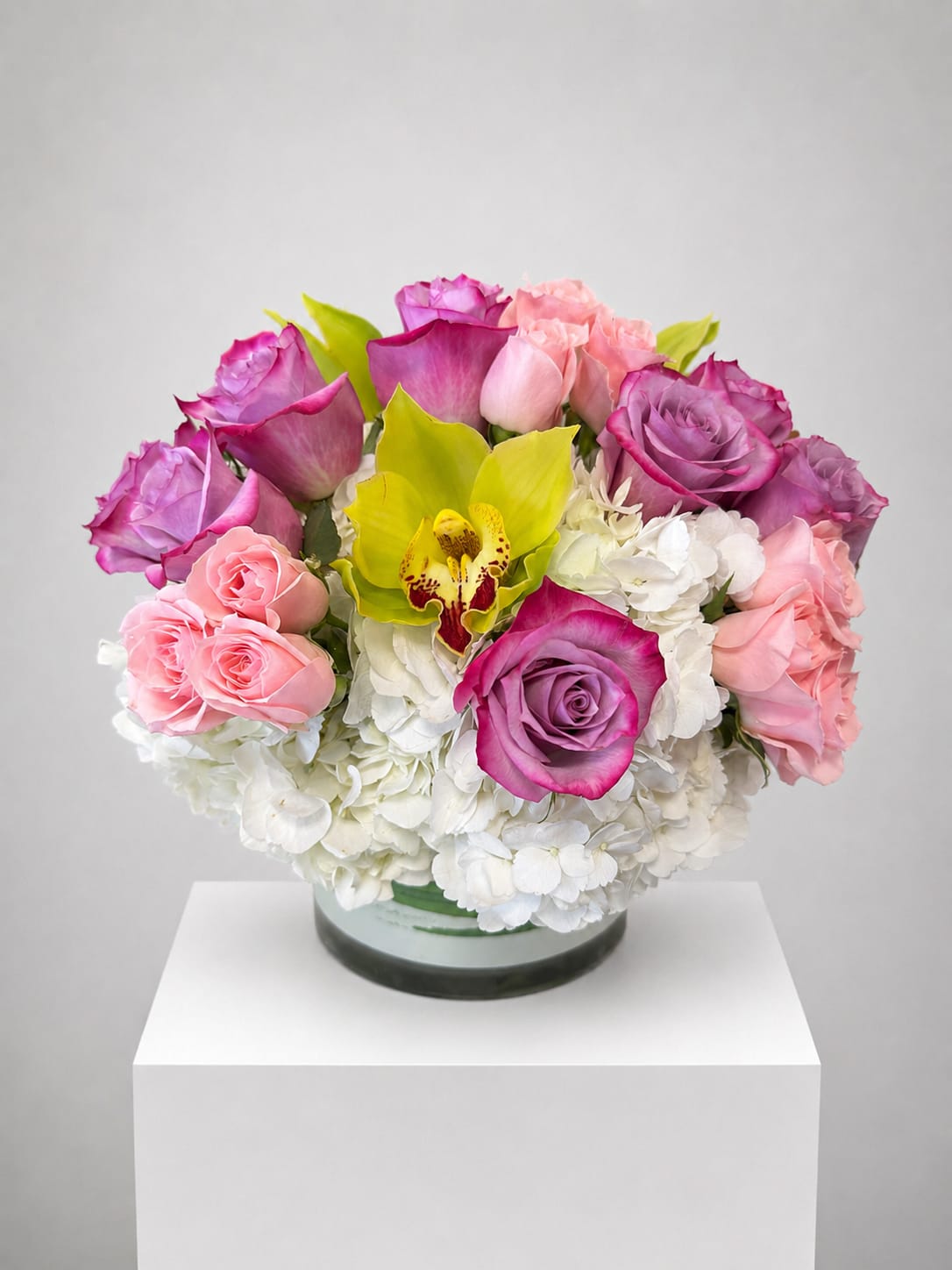 Round bouquet of pink and purple roses with white hydrangeas in a glass vase