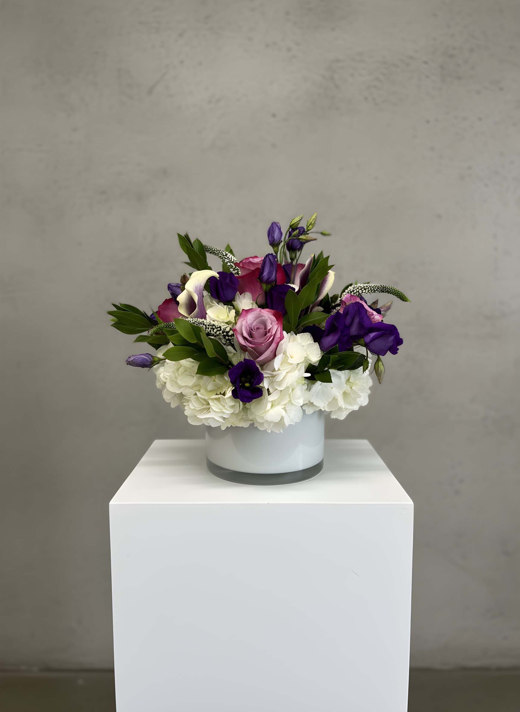 Valora - Graceful, sophisticated, and effortlessly elegant, Valora is a premium floral arrangement designed to leave a lasting impression. Featuring luxurious lavender roses, rich purple lisianthus, elegant white calla lilies, lush white hydrangeas, and fresh seasonal greenery, this handcrafted bouquet is artfully arranged in a modern white glass cylinder vase for a clean, contemporary look.  Perfect for birthdays, anniversaries, sympathy, celebrations, thank-you gifts, or simply letting someone know you're thinking of them, Valora brings timeless beauty to any occasion. Every arrangement is designed by the experienced floral designers at All Occasions Florist using the freshest flowers available to ensure exceptional quality and long-lasting beauty.  We proudly offer same-day flower delivery in Dallas, TX, as well as delivery throughout Highland Park, University Park, Preston Hollow, Uptown Dallas, Lakewood, Richardson, Plano, Garland, and many surrounding communities. Whether you're sending flowers to a home, office, hospital, funeral home, or event venue, Valora is a beautiful choice for any meaningful moment.  Order Valora online today from All Occasions Florist, your trusted Dallas florist for luxury flower arrangements, premium floral designs, and reliable same-day flower delivery.